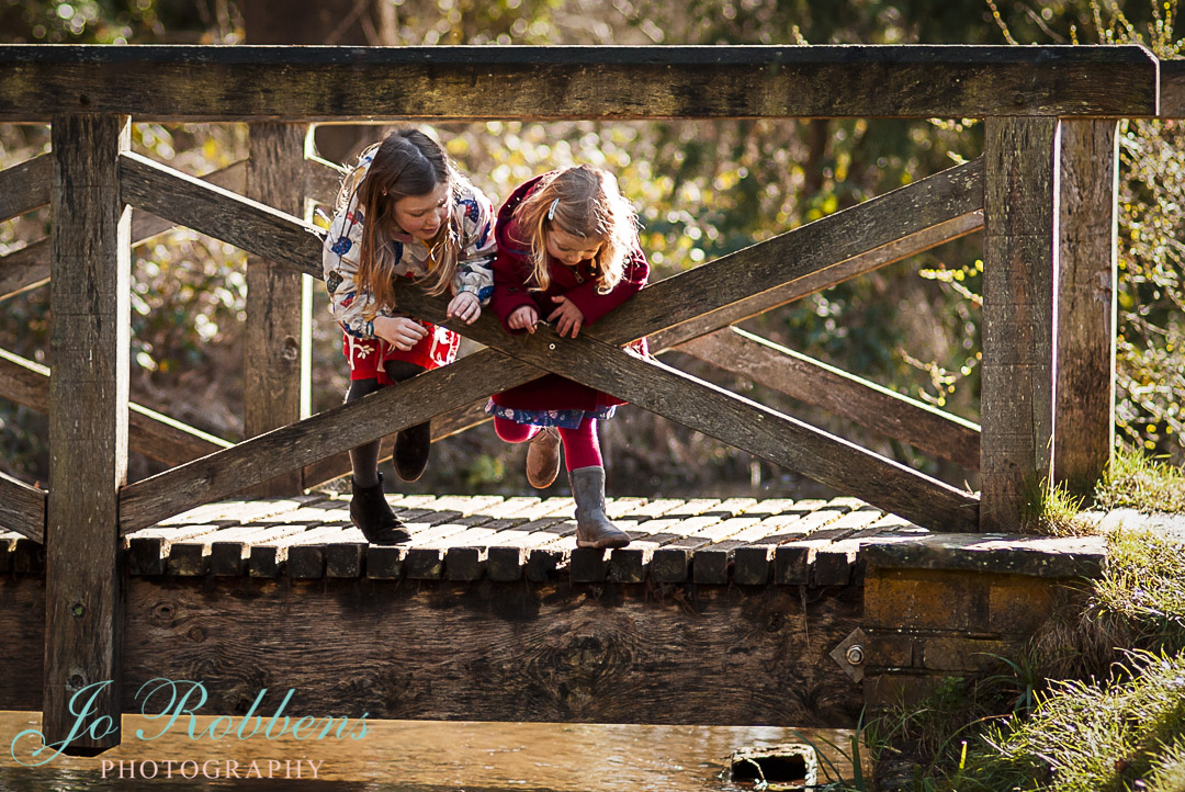 Two children playing pooh sticks in beautiful light